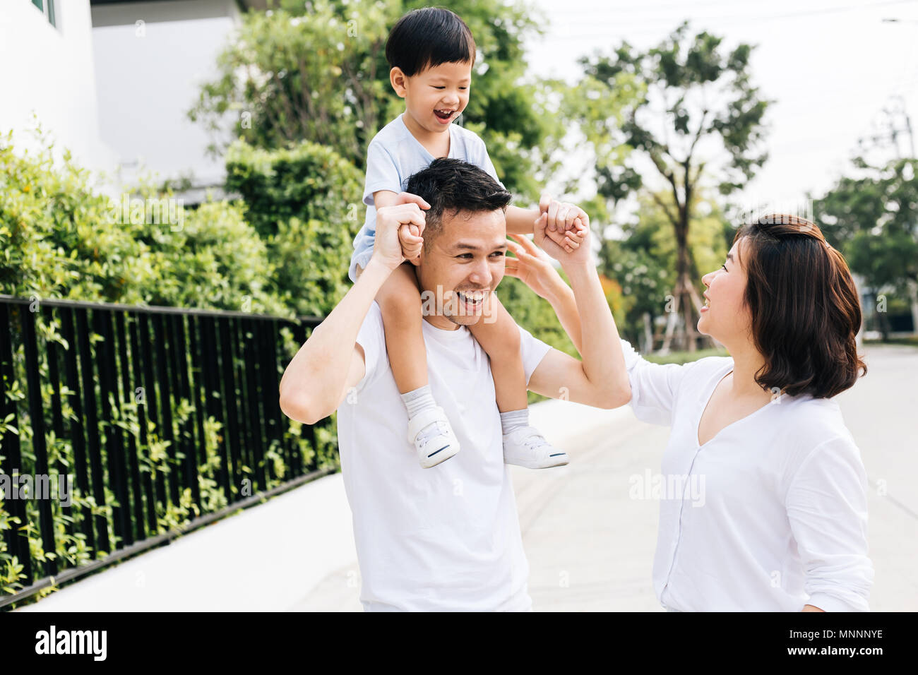 Cute Asian father piggybacking his son along with his wife in the park. Excited family spending time together with happiness Stock Photo