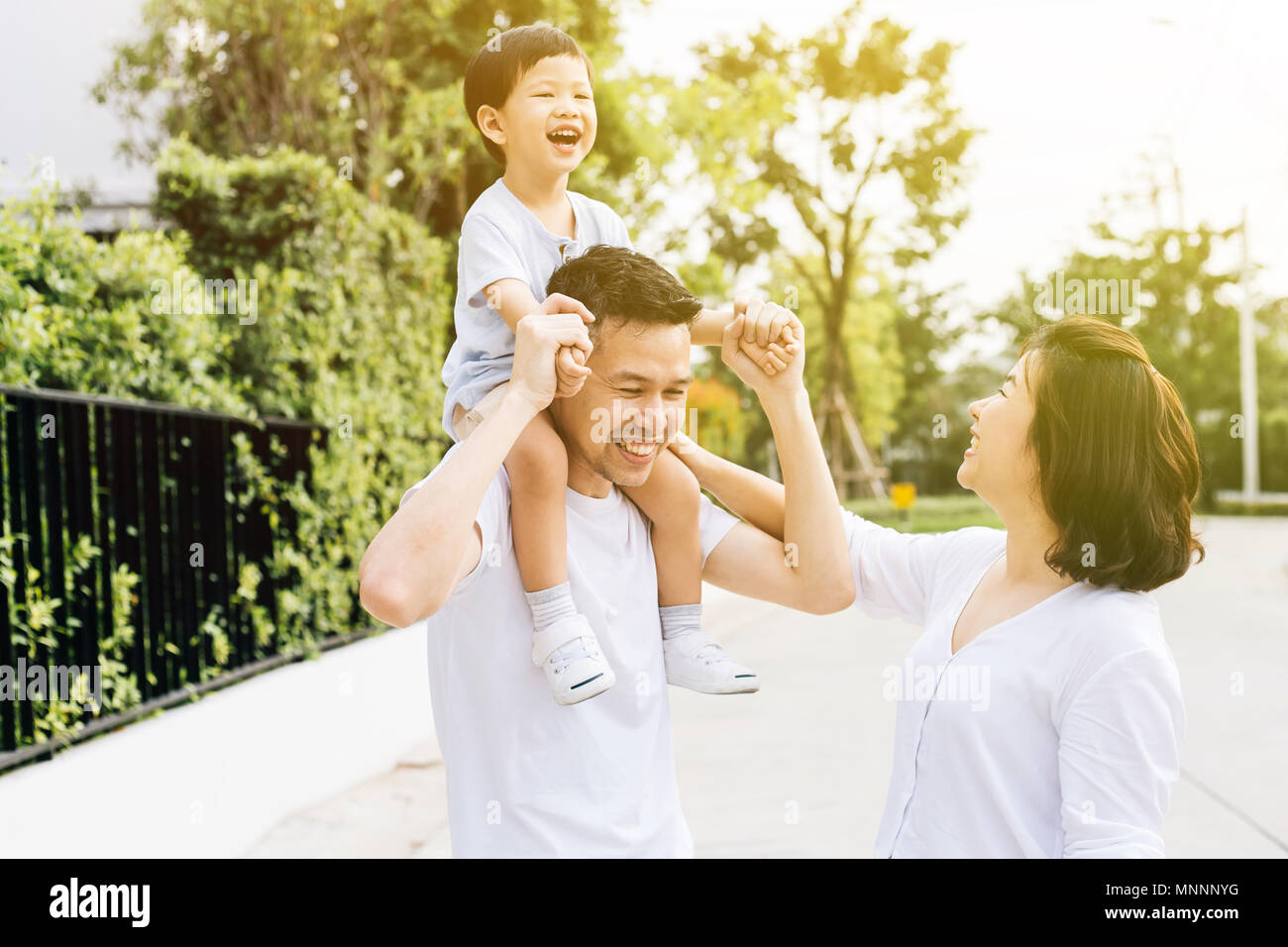 Cute Asian father piggybacking his son along with his wife in the park. Excited family spending time together with happiness Stock Photo