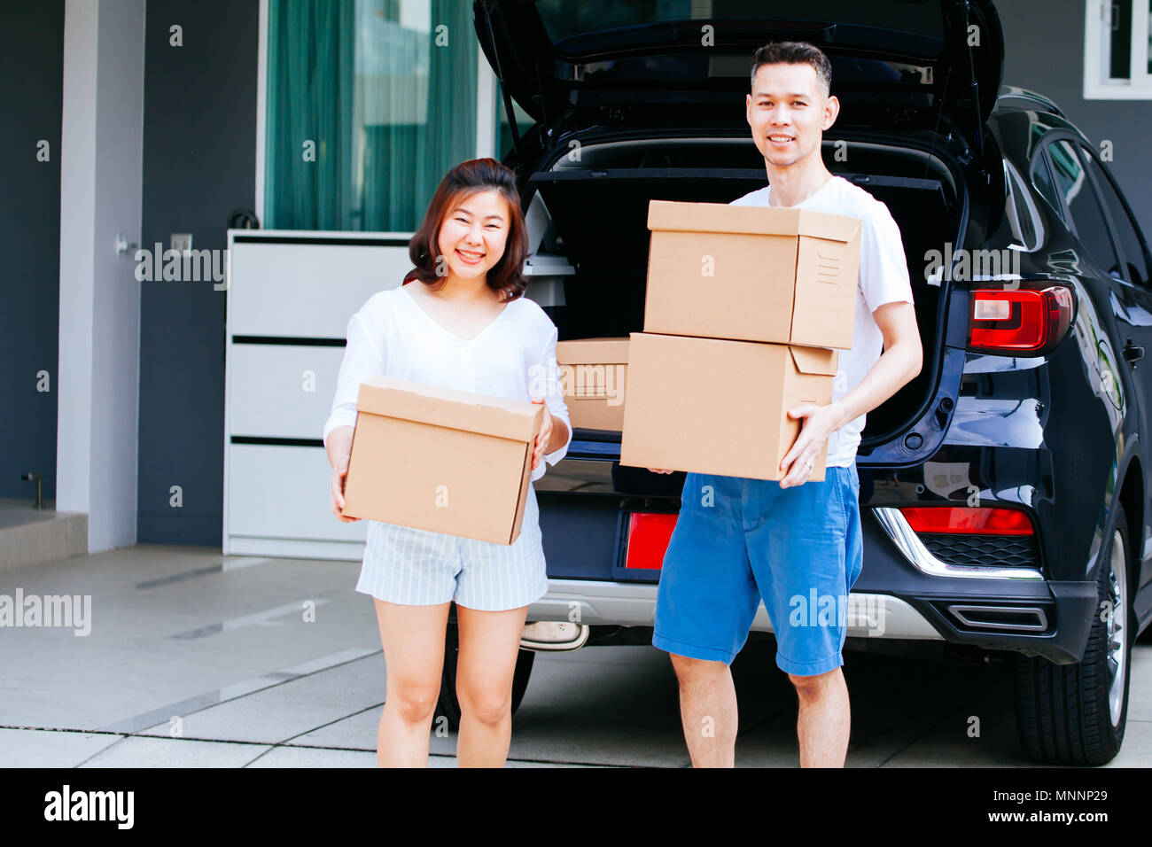 Mature happy Asian married couple carrying cardboard boxes from car ...