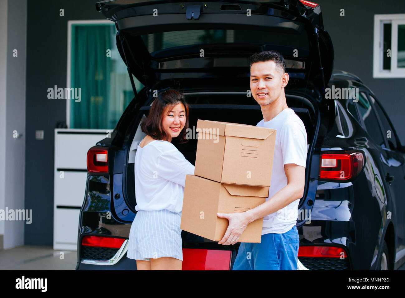 Mature happy Asian married couple carrying cardboard boxes from car ...