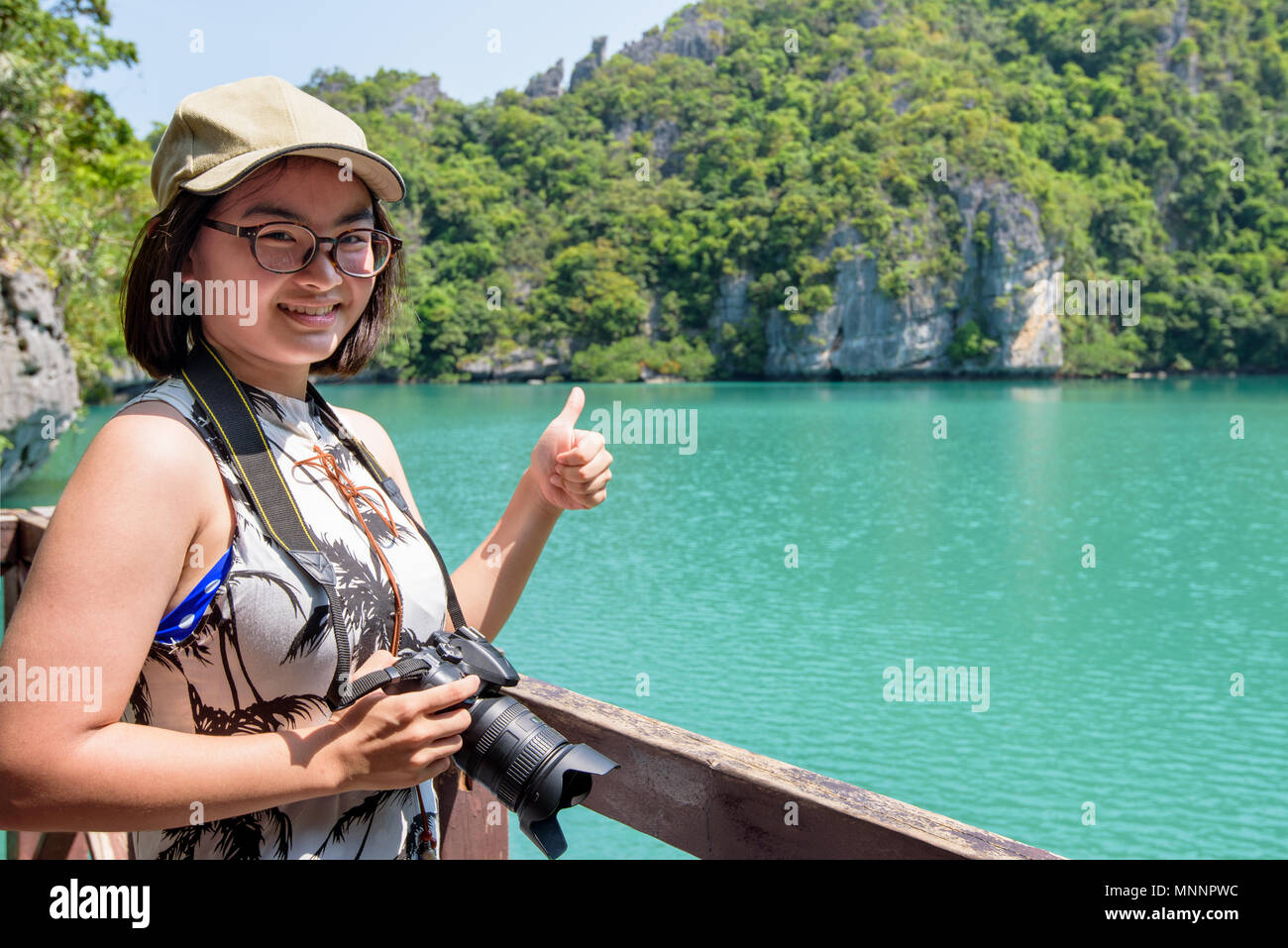 Woman tourist at Thale Nai holding dslr camera and thumbs up after taking pictures of Blue Lagoon (Emerald Lake) on Koh Mae Ko island viewpoint in Mu  Stock Photo