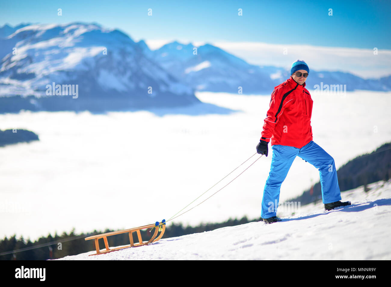 Young attractive man ready to go sledding in Swiss Alps during winter vacation. Stock Photo