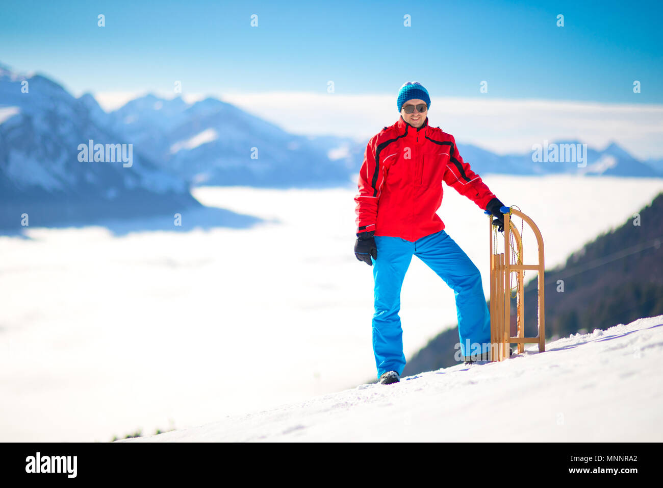 Young attractive man ready to go sledding in Swiss Alps during winter holiday. Stock Photo
