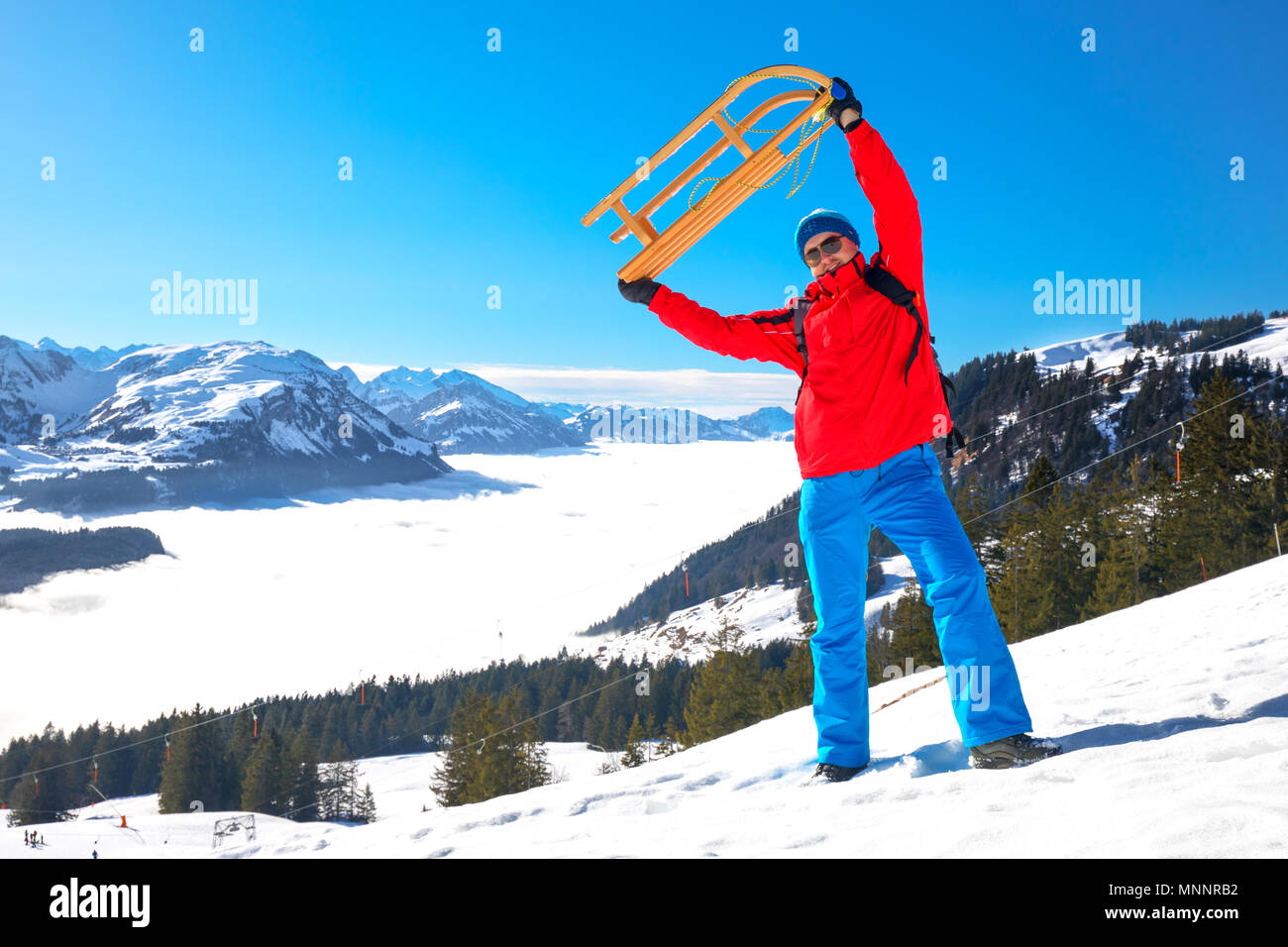 Young attractive man ready to go sledding in Swiss Alps during winter vacation. Stock Photo