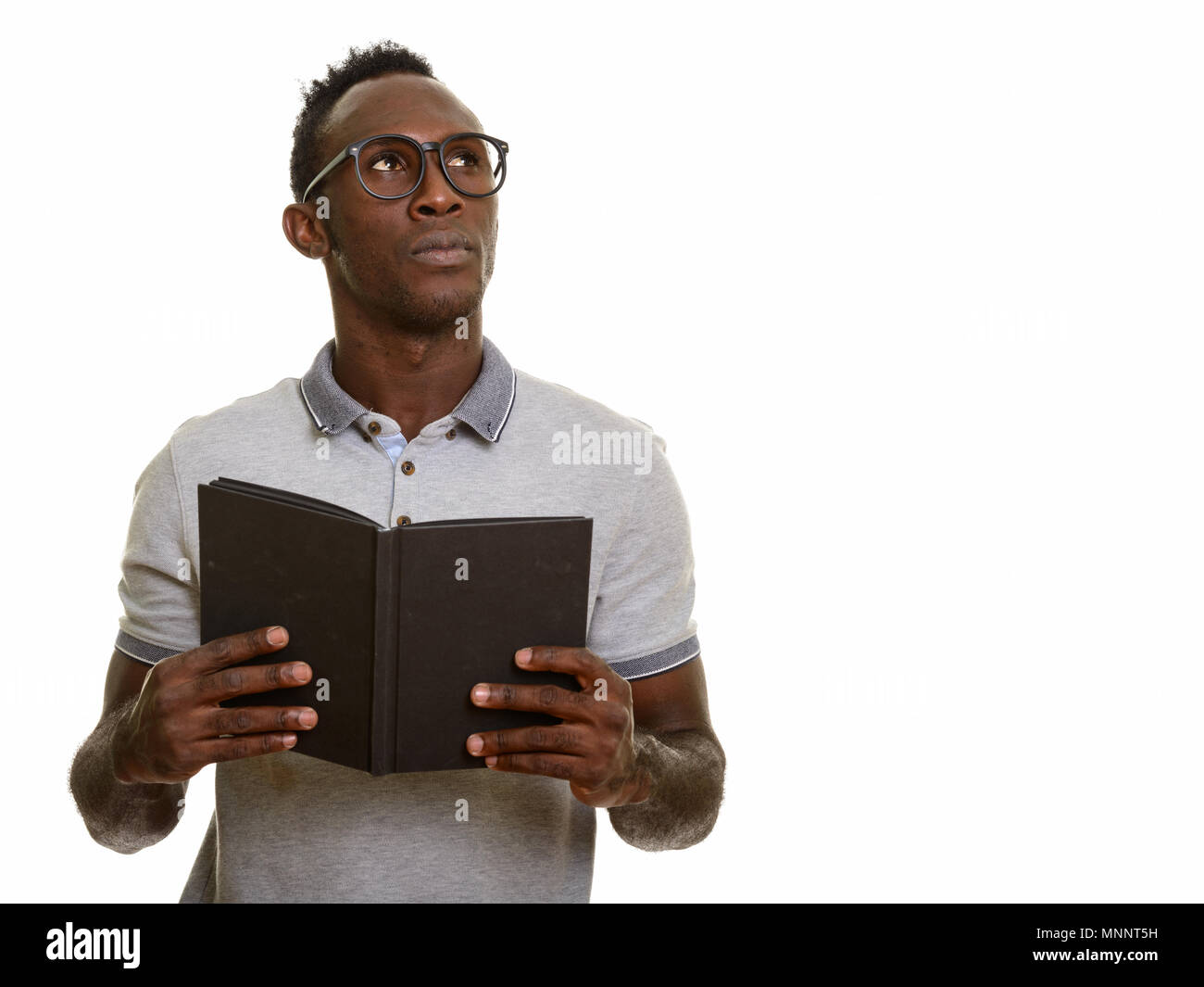 Young black African man holding book while thinking Stock Photo