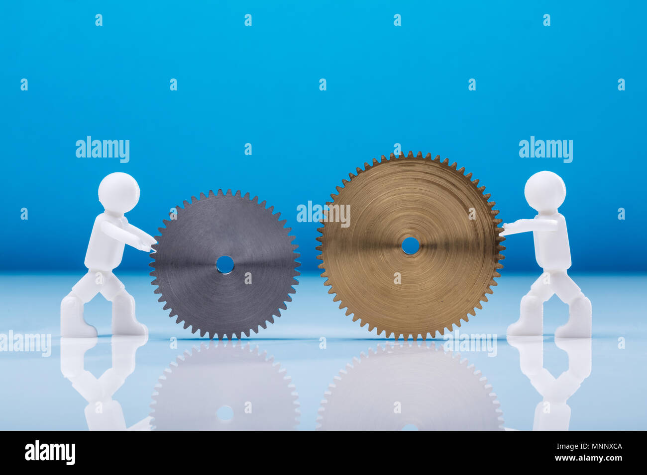 Side View Of Two White Human Figures Holding Cogwheels Against Blue Background Stock Photo