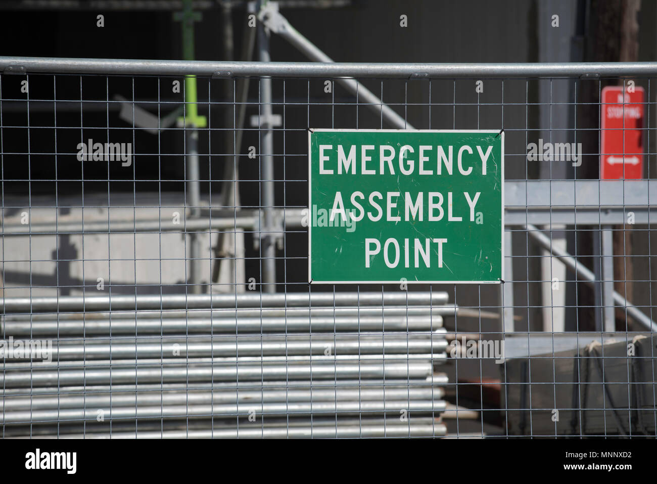 An Emergency Assembly Point sign pinned to temporary fencing in front of alloy scaffolding on a construction work site in Australia Stock Photo