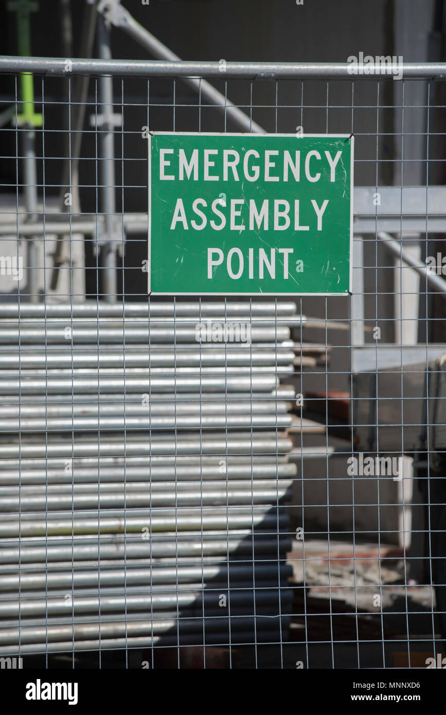 An Emergency Assembly Point sign pinned to temporary fencing in front of alloy scaffolding on a construction work site in Australia Stock Photo