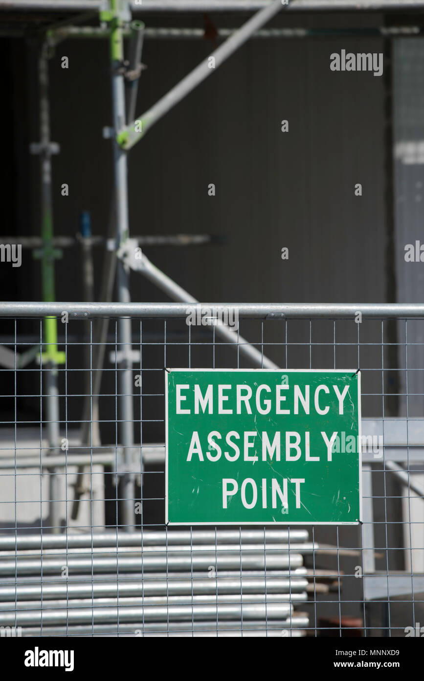 An Emergency Assembly Point sign pinned to temporary fencing in front of alloy scaffolding on a construction work site in Australia Stock Photo