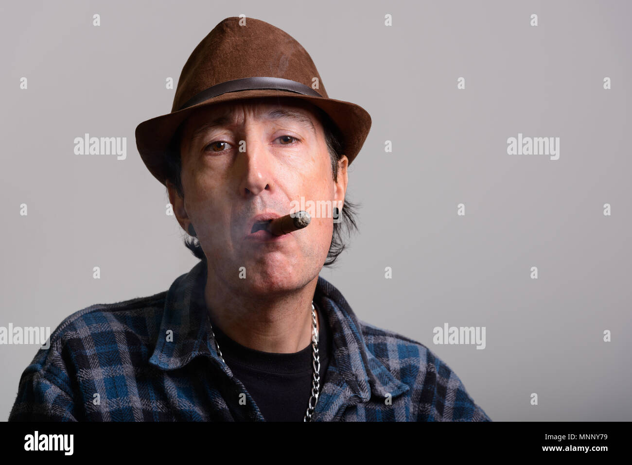 Studio shot of mature gangster man smoking cigar Stock Photo