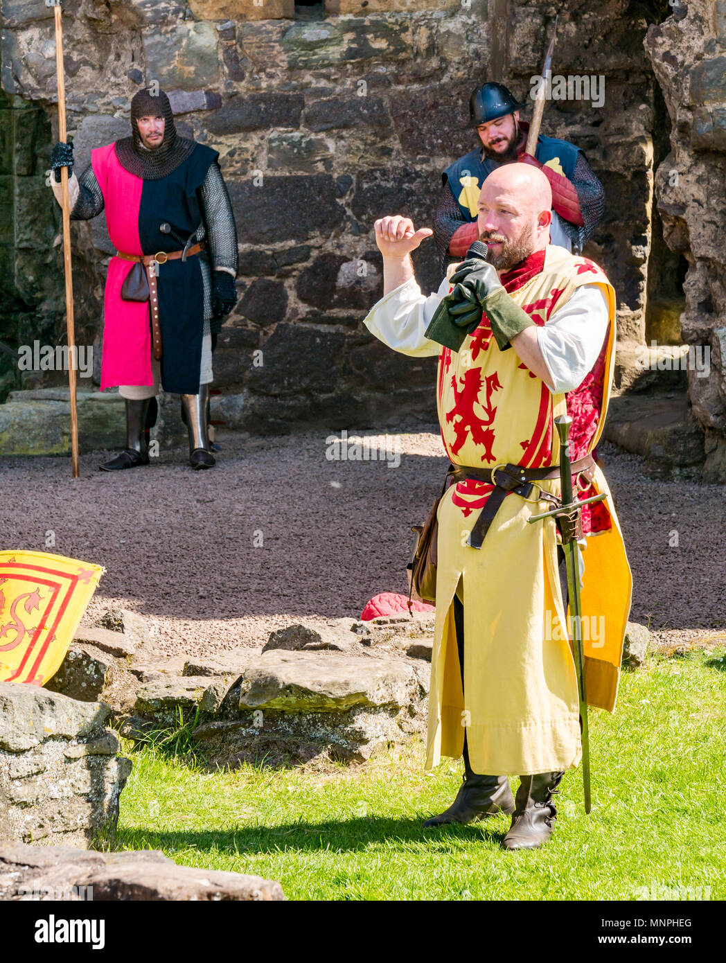 Dirleton, East Lothian, Scotland, UK, 19th May 2018.  Dirleton, East Lothian, Scotland, UK, 19th May 2018.  Dirleton Castle attack re-enactment. The Historic Saltire Society staging a tongue-in-cheek re-enactment of an attack by Robert the Bruce, King of Scotland, around 1311, to take the castle from the English, dressed in authentic clothes and armour and wielding replica weapons in Historic Environment Scotland's Dirleton Castle. A man playing Robert the Bruce dressed in costume with a lion rampant speaking to the crowd with a microphone. Soldiers with pikes are in the background Stock Photo