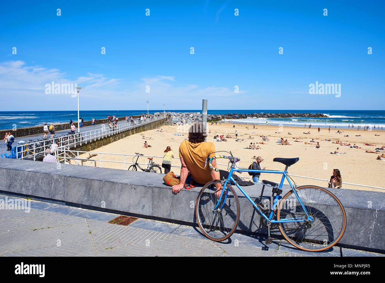 San Sebastian, Spain - May 11, 2018. A young men with their bike parked in front of  Zurriola beach and Monte Ulia in background at sunny day. San Seb Stock Photo
