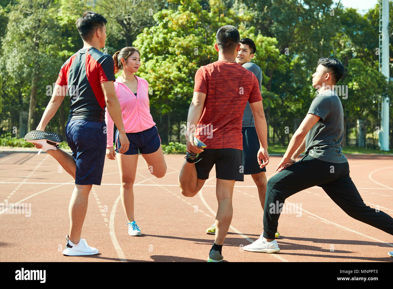 four asian young adults warming up stretching legs on track. Stock Photo