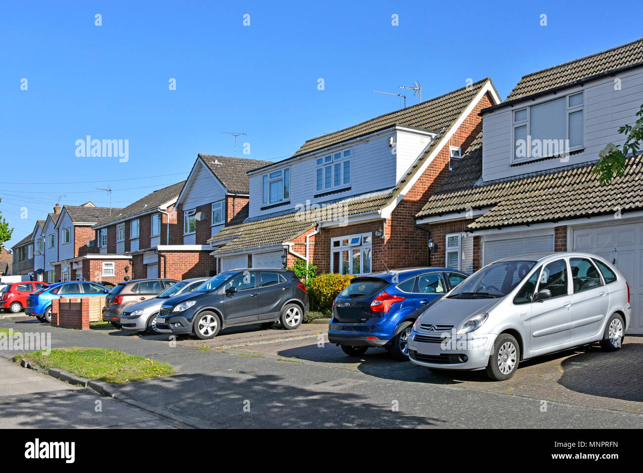 Suburb street scene row semi detached houses paving over front garden with paved driveway replacing house lawn for car parking space Essex England UK Stock Photo