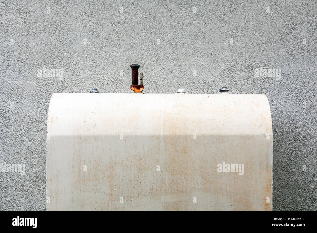 old weathered oil taink against a white stucco wall Stock Photo