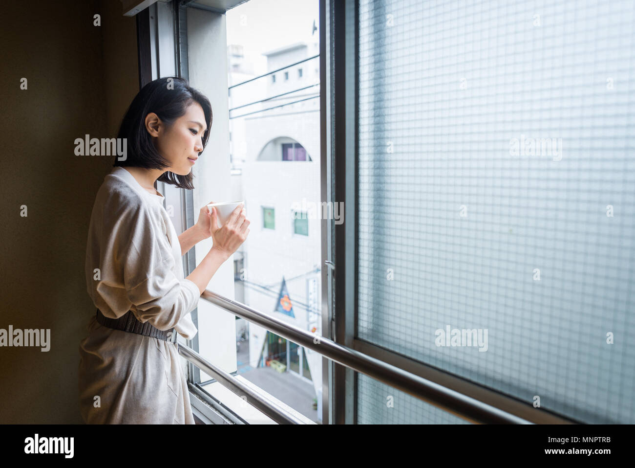 Japanese woman sitting in a traditional Tokyo apartment and drinking a cup ...