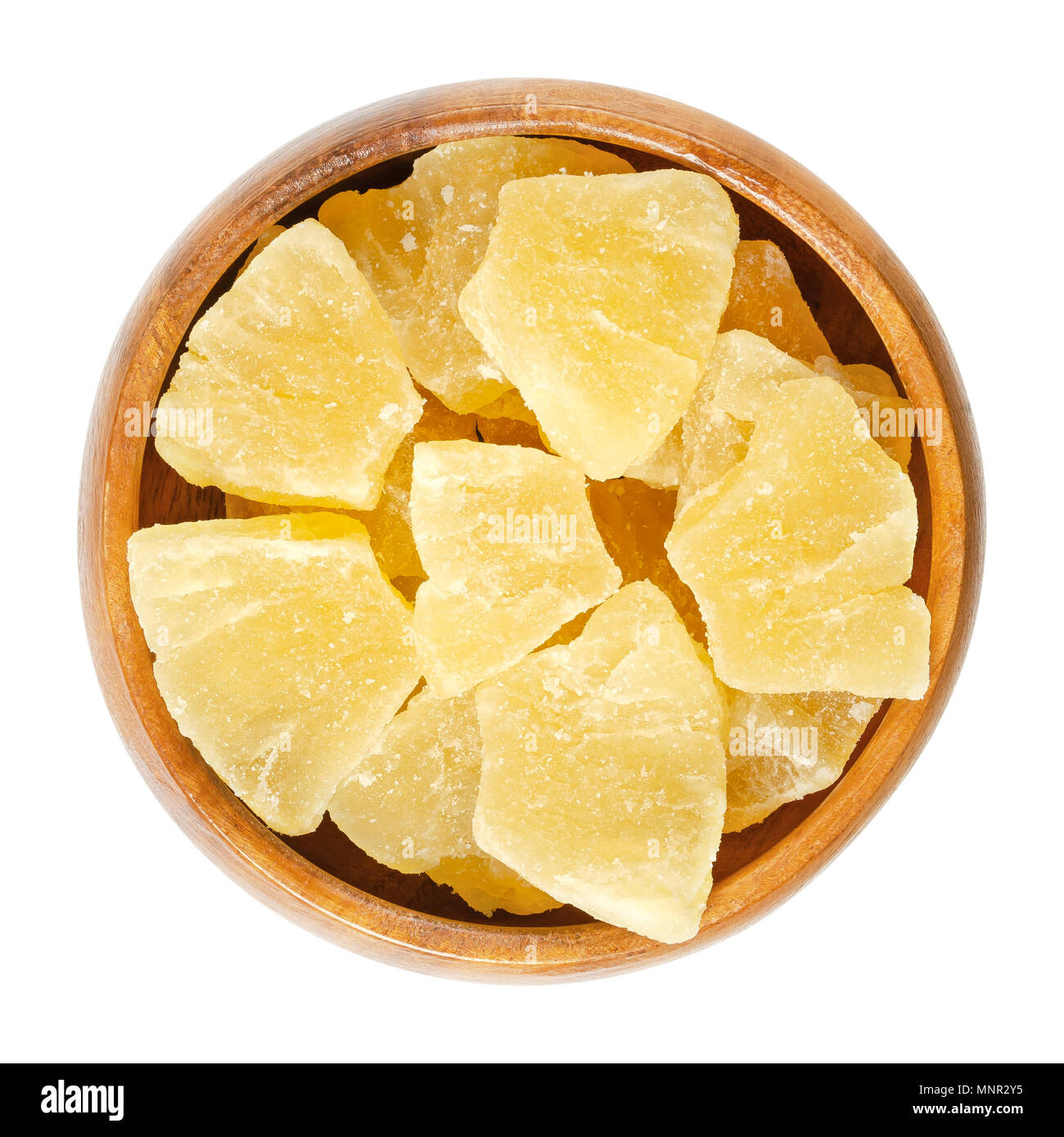 Candied pineapple pieces in wooden bowl. Crystallized chunks of Ananas comosus. Yellow colored flesh of the fruit preserved with sugar. Snack. Stock Photo