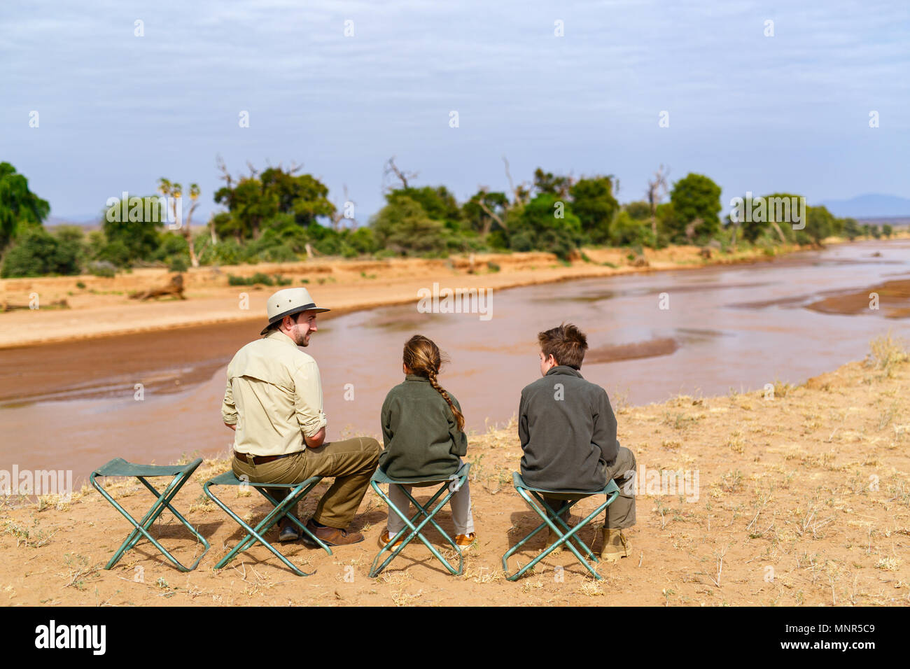 Family of father and kids on African safari vacation enjoying Ewaso Nyiro River views in Samburu Kenya Stock Photo