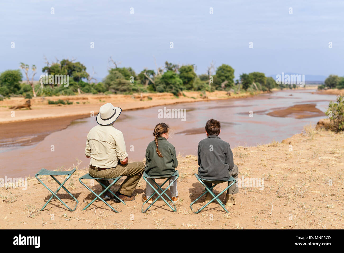 Family of father and kids on African safari vacation enjoying Ewaso Nyiro River views in Samburu Kenya Stock Photo