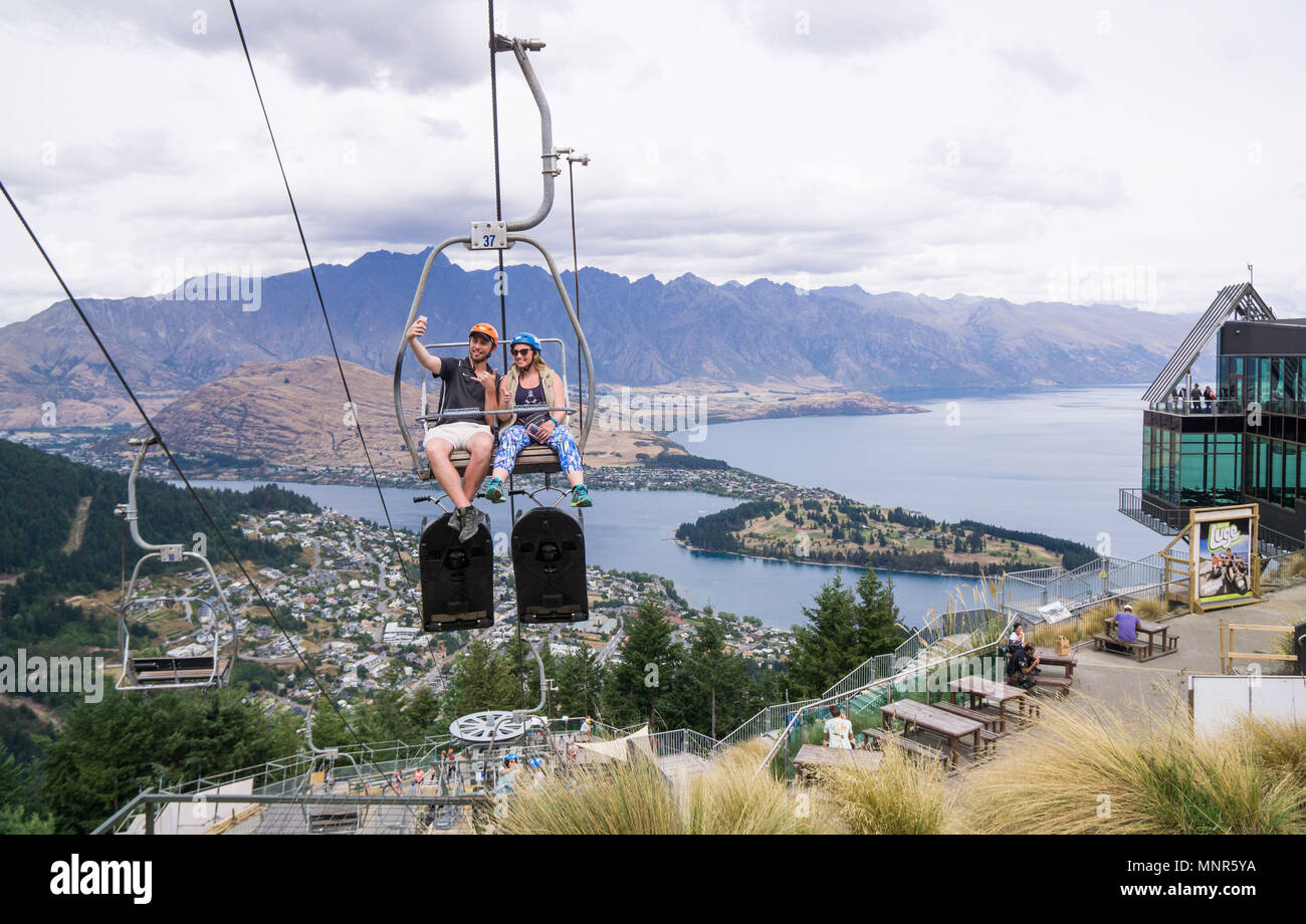 A young couple taking a selfie on the Skyline Gondola chairlift in Queenstown, NZ Stock Photo