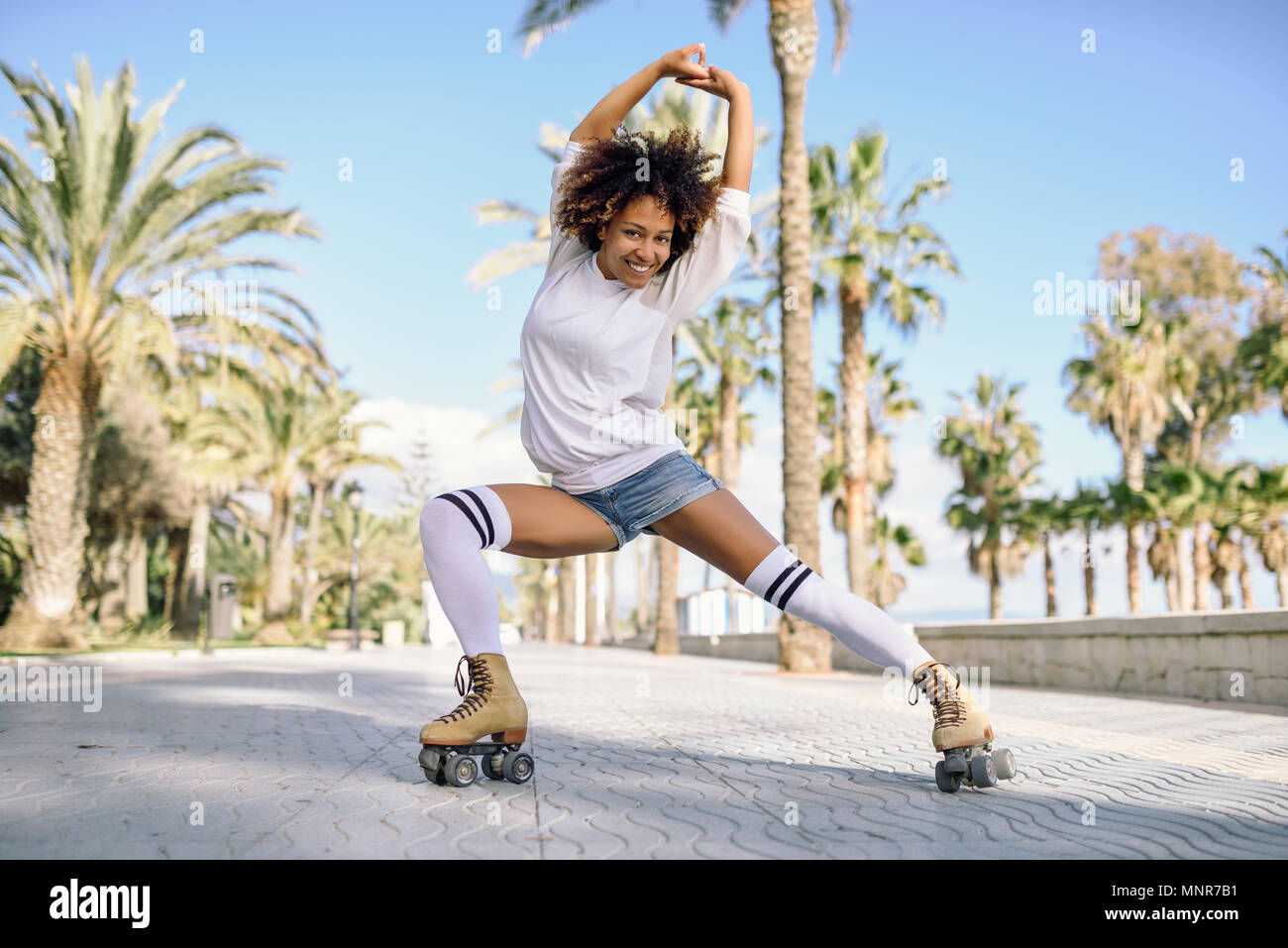 Smiling black woman on roller skates riding outdoors on beach promenade