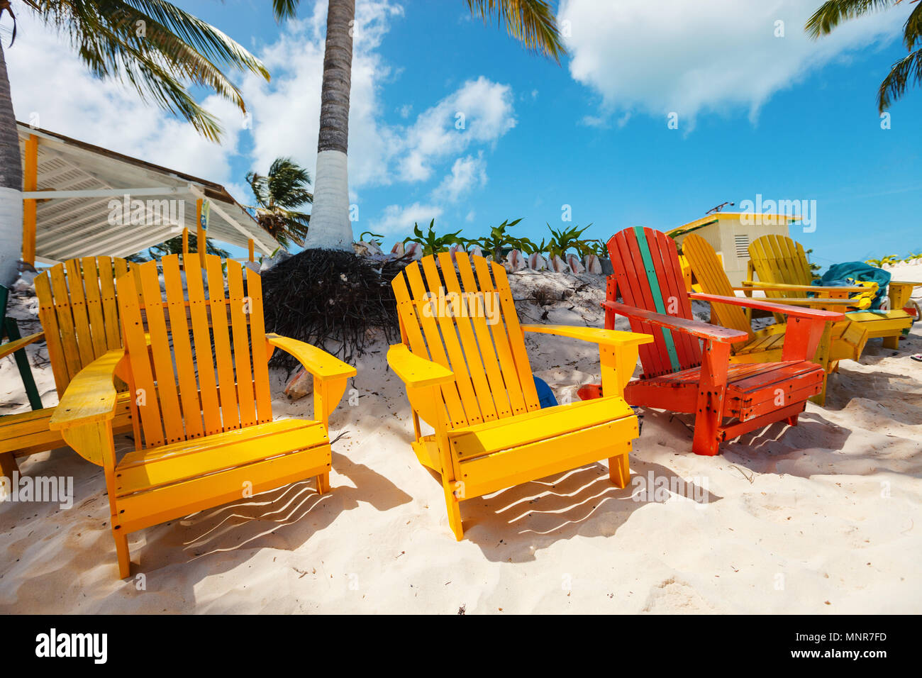 Colorful adirondack yellow and orange lounge chairs at tropical beach in Caribbean with beautiful turquoise ocean water, white sand and blue sky Stock Photo