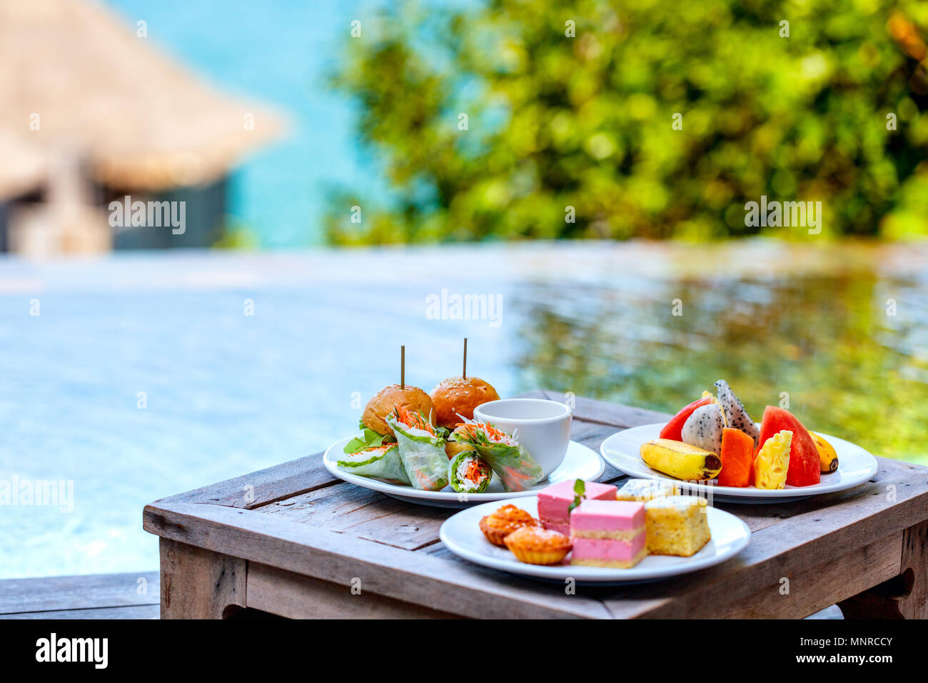 Room service delicious lunch burgers,  fruits and sweets served on a table near swimming pool Stock Photo