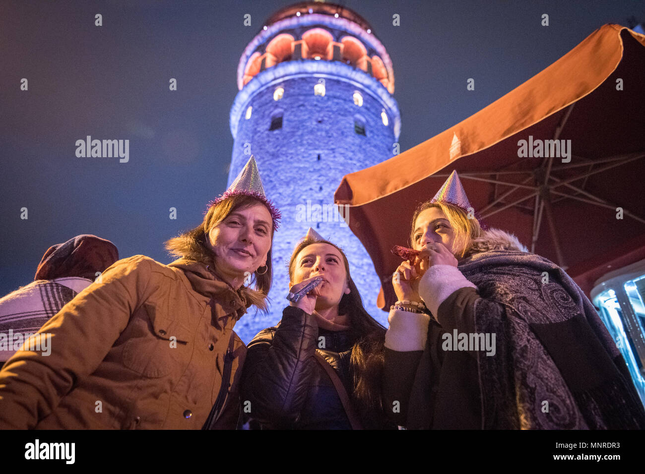 Group of woman stand under the illuminated Galata Kulesi, a medieval tower built by the Byzantines, wearing party hats and ready to celebrate in Istan Stock Photo