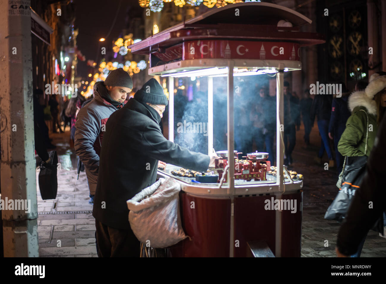 Two street vendors stand by food cart roasting chestnuts with fluorescent lights illuminated steam, Istanbul, Turkey Stock Photo