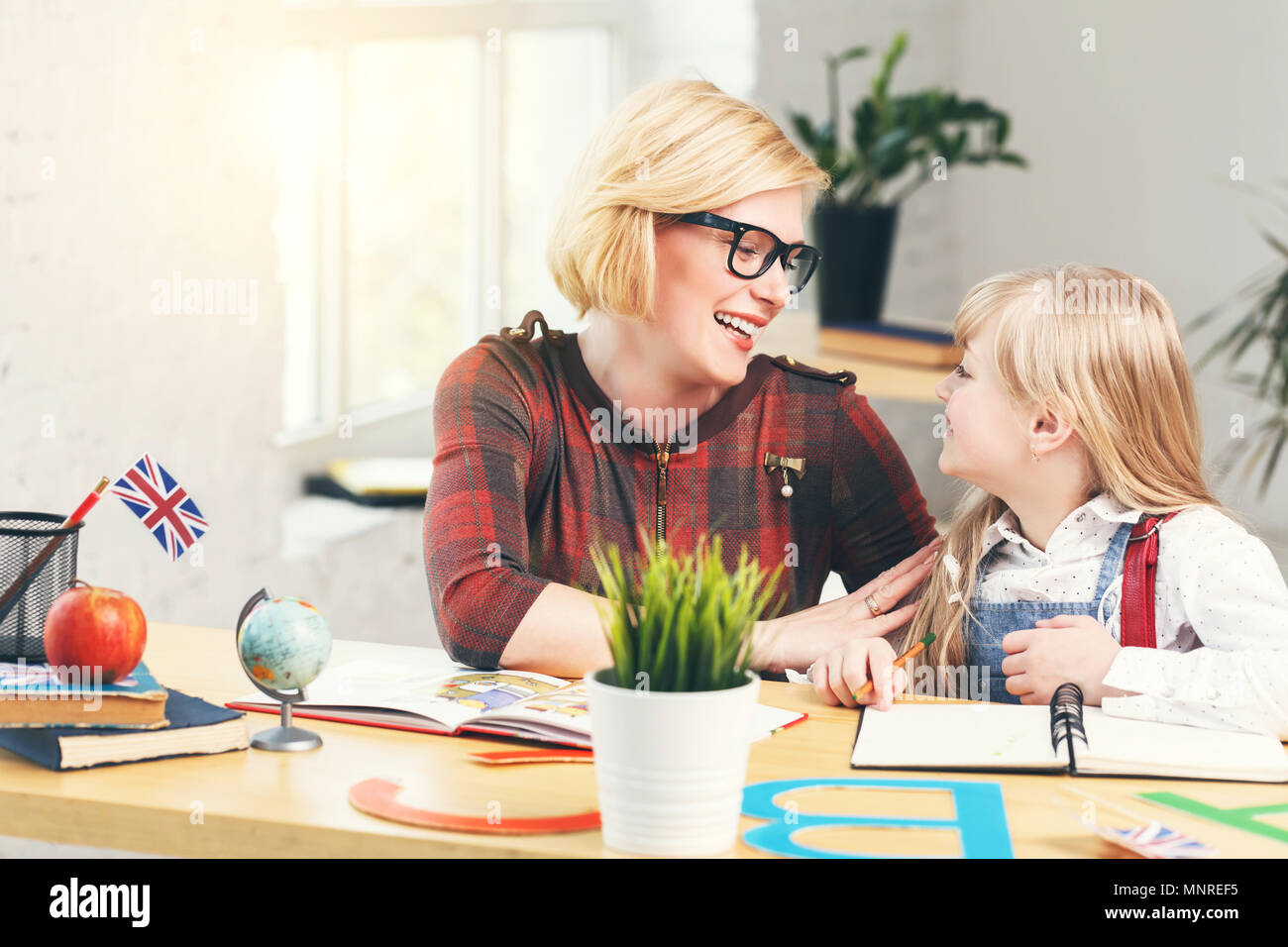 School kid girl studying English language with female educator, table