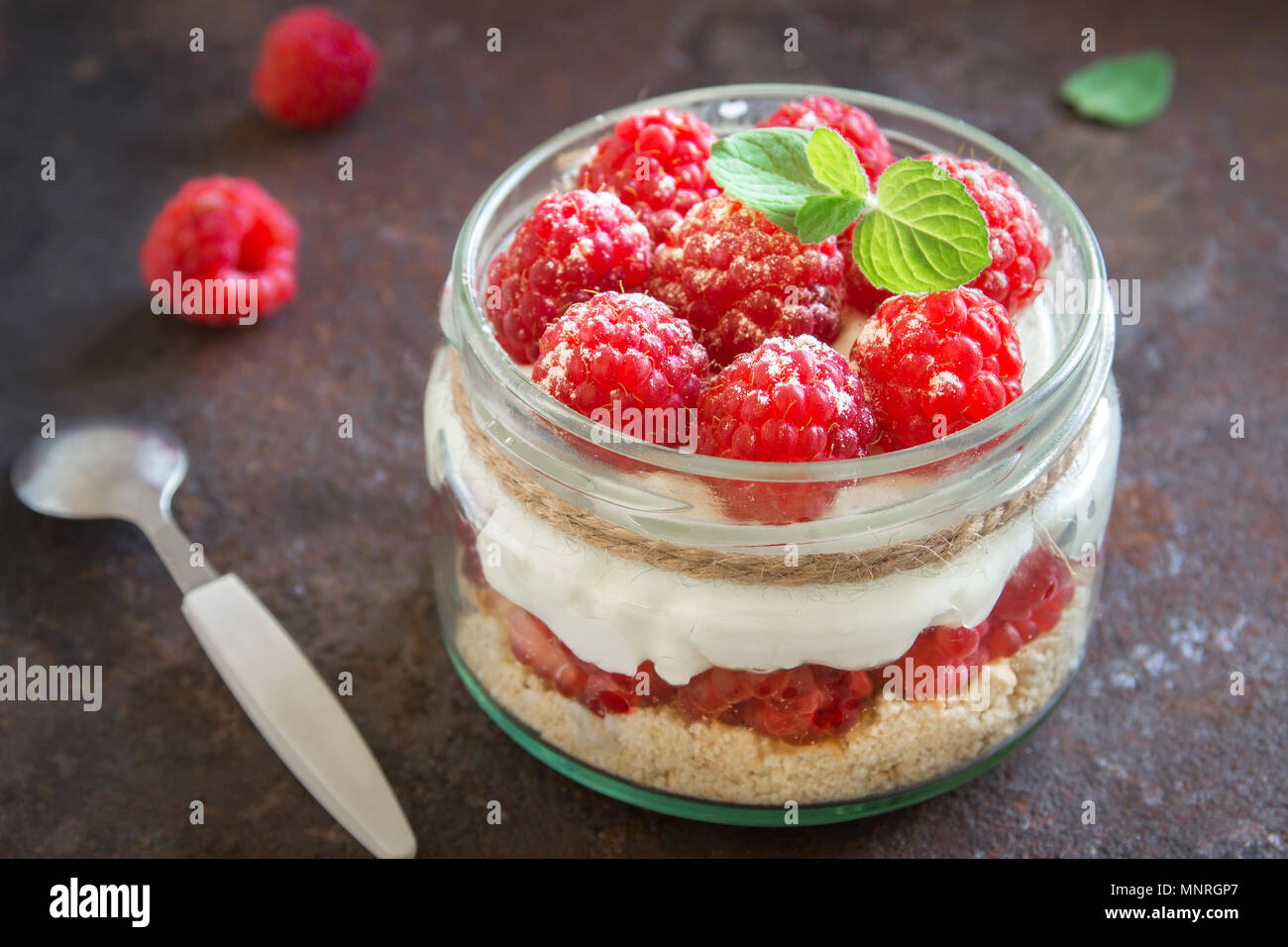 Raspberry cheesecake in glass jar with fresh raspberries and cream cheese  on rustic metal background. Healthy homemade summer berry layered dessert. Stock Photo