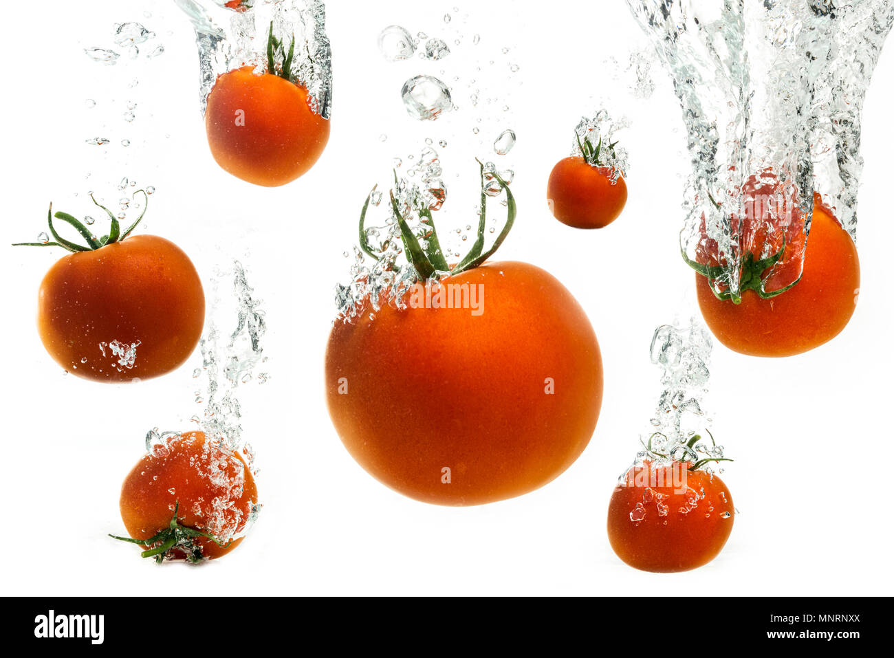Tomatoes falling into crystal clear water splashing with air bubbles