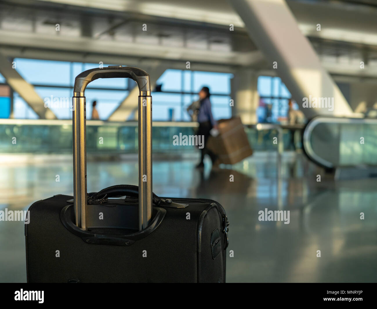Black carry on luggage sitting at clean modern airport with workers in