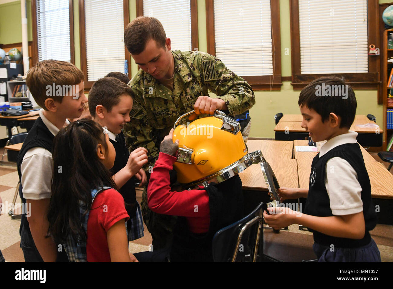 Wash. (March 14, 2018) -- Navy Diver 2nd Class Matthew Sanders, from Louisville, Kentucky, assigned to Puget Sound Naval Shipyard and Intermediate Maintenance Facility's Everett dive locker, lets a group of 1st grade students from Immaculate Conception and Our Lady Of Perpetual Help School try on a dive-helmet after during a Science, Technology, Engineering and Math - Art + Design (STEAM) presentation about how science and math are factored into the process of diving. STEAM is a program that teaches children the importance of science, technology, engineering, math, art and design in the everda Stock Photo