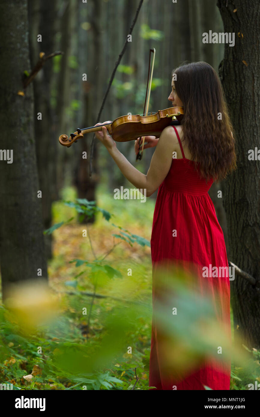 Girl in a red dress playing the violin in the woods, soft light Stock ...
