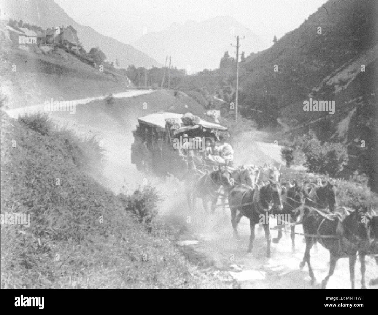 A Stagecoach. Engins’ road. Stagecoach downhill pulled by eight horses in the dust. Travellers have sat next the coach. There are luggage on the roof. The path winds through a mountainous landscape. On the bottom sides are electric poles. Some houses are located on a mountainside. 1906. Unknown 963 Patache. Route d'Engins Stock Photo
