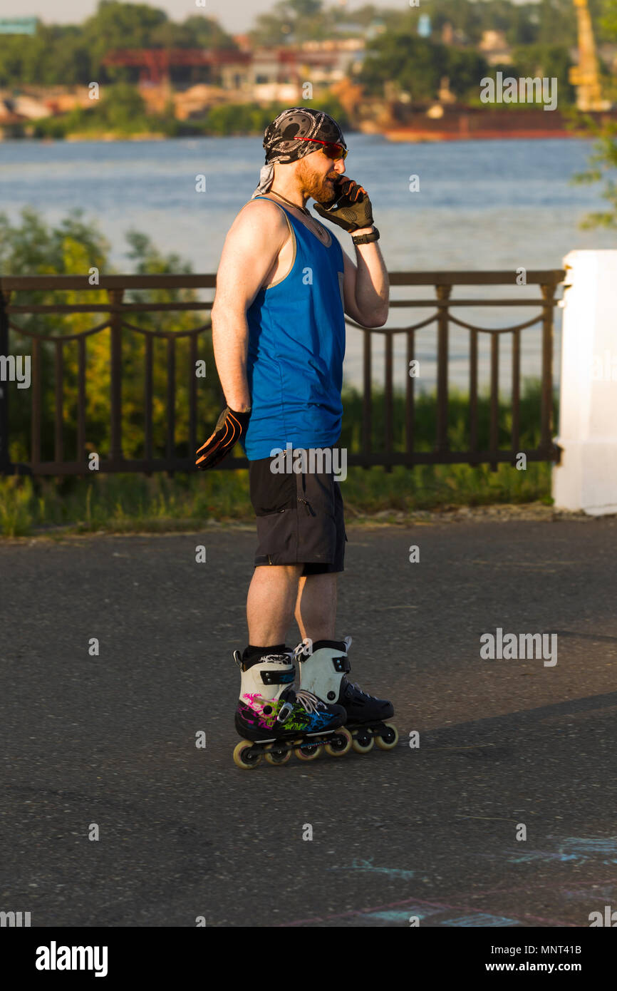 Man talking on cell phone, riding on roller skates, lit by sunlight Stock Photo