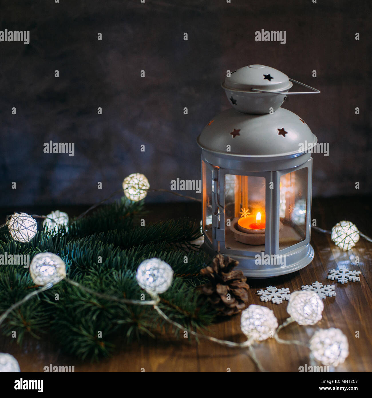Cozy winter home. Lantern, candle, garland, snowflakes, cone, sprig of Christmas tree on wooden table. The atmosphere of a New Year's fairy tale. Plac Stock Photo
