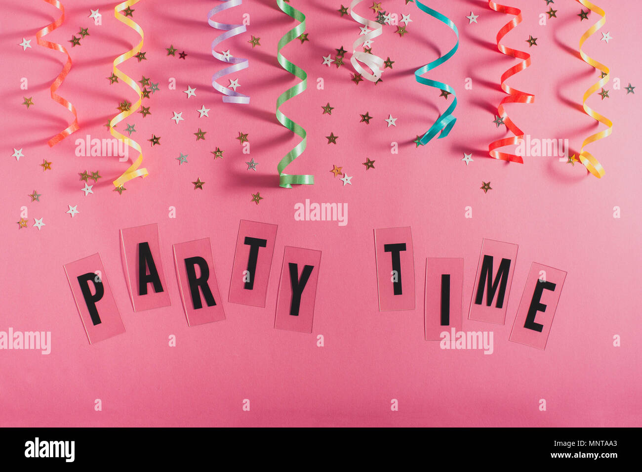Colorful party streamers, gold little stars and text Party time on pink background. Girly birthday concept. Flat lay. Stock Photo