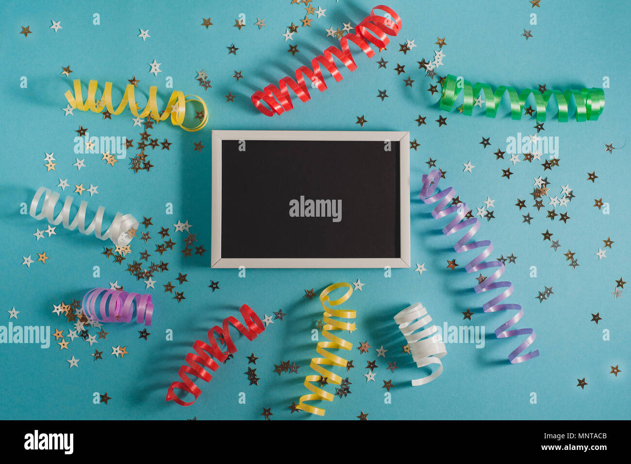 Colorful party streamers, gold little stars and blackboard for text on blue backgrond. Party or birthday concept. Stock Photo