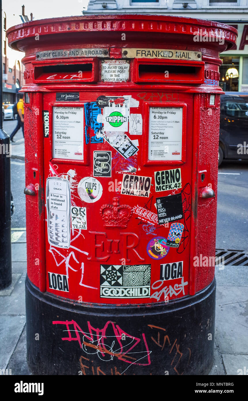 A graffiti and sticker decorated Royal Mail post box on Old Compton Street in London's fashionable Soho entertainment district Stock Photo