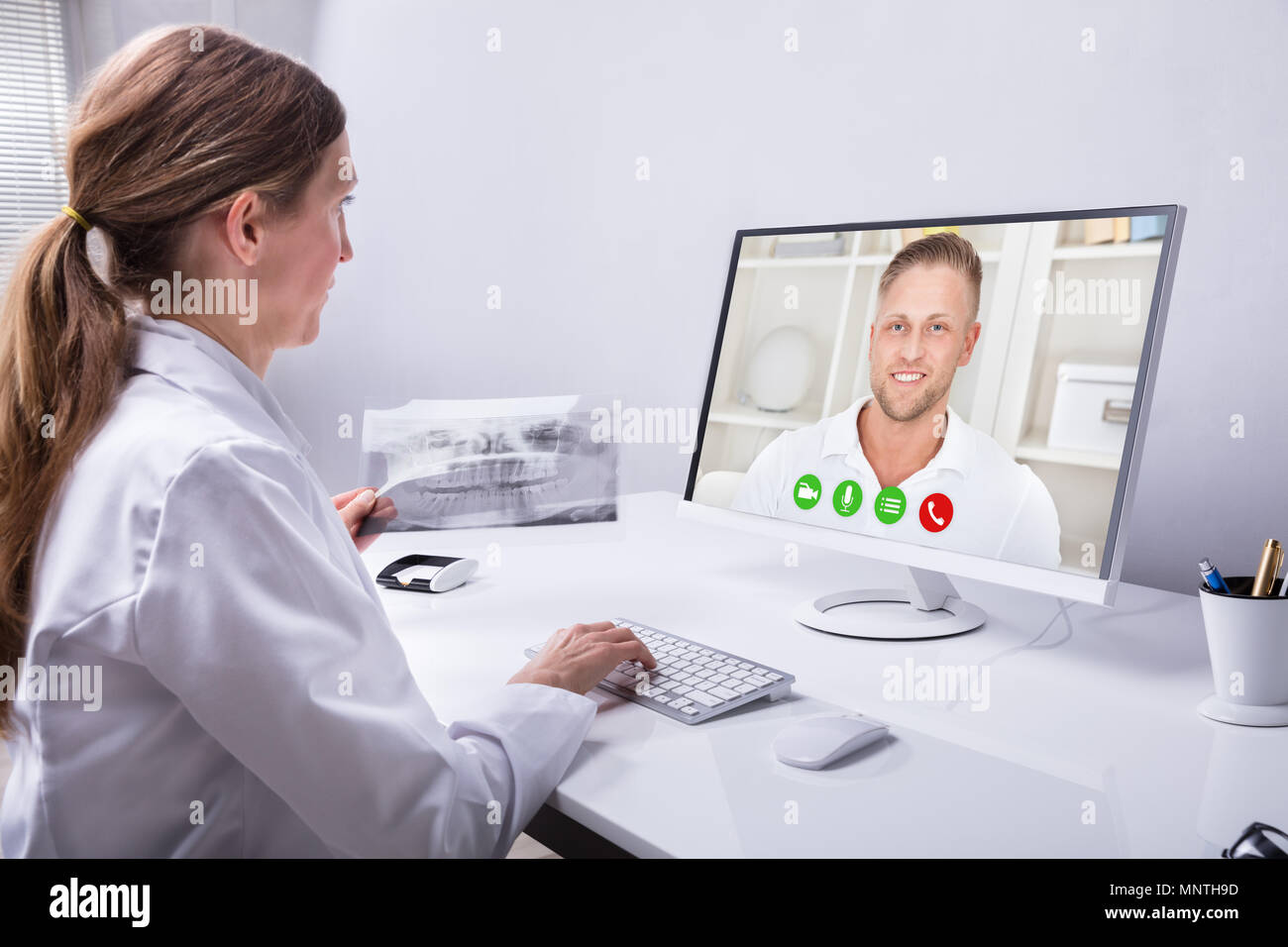 Dentist Holding Teeth X-ray While Video Conferencing With Man On Computer Stock Photo