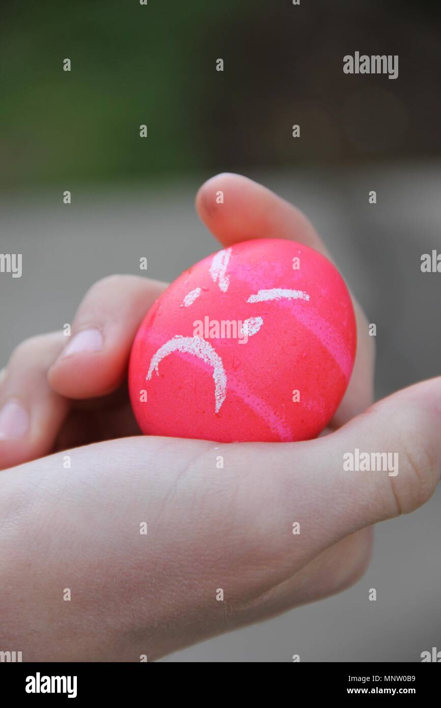 Bright pink angry Easter egg in a child's hand on Easter morning. Stock Photo