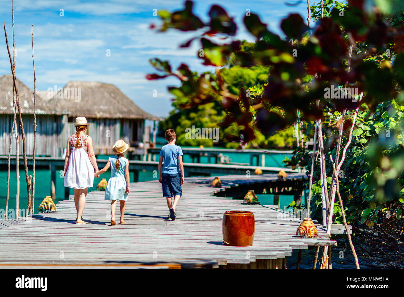 Back view of happy beautiful family walking on wooden jetty during summer vacation at luxury resort Stock Photo