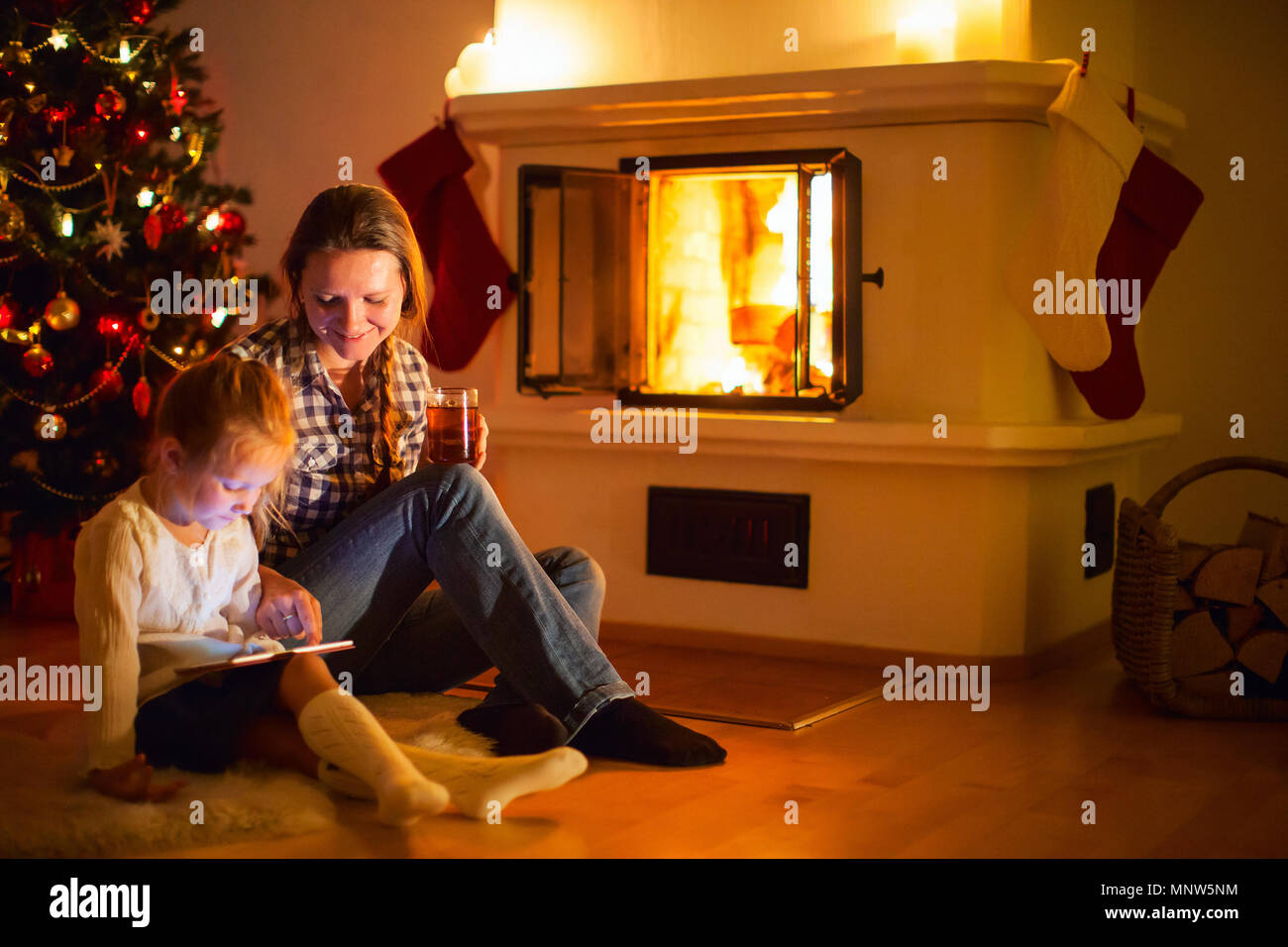 Mother and daughter sitting by a fireplace in their family home on winter Stock Photo