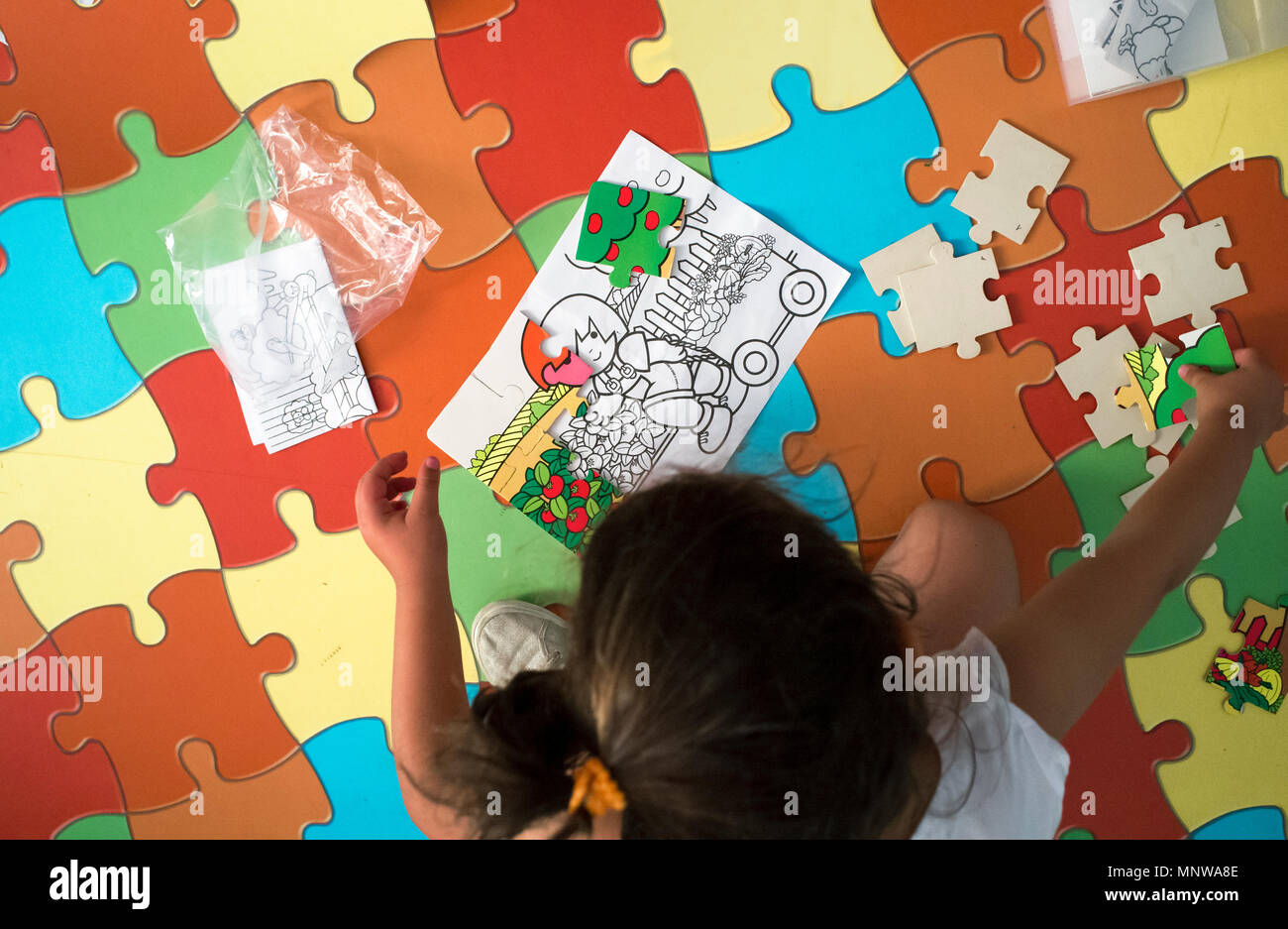 Child girl playing with puzzle over puzzle carpet. Overhead shot. Soft noise at 100% Stock Photo