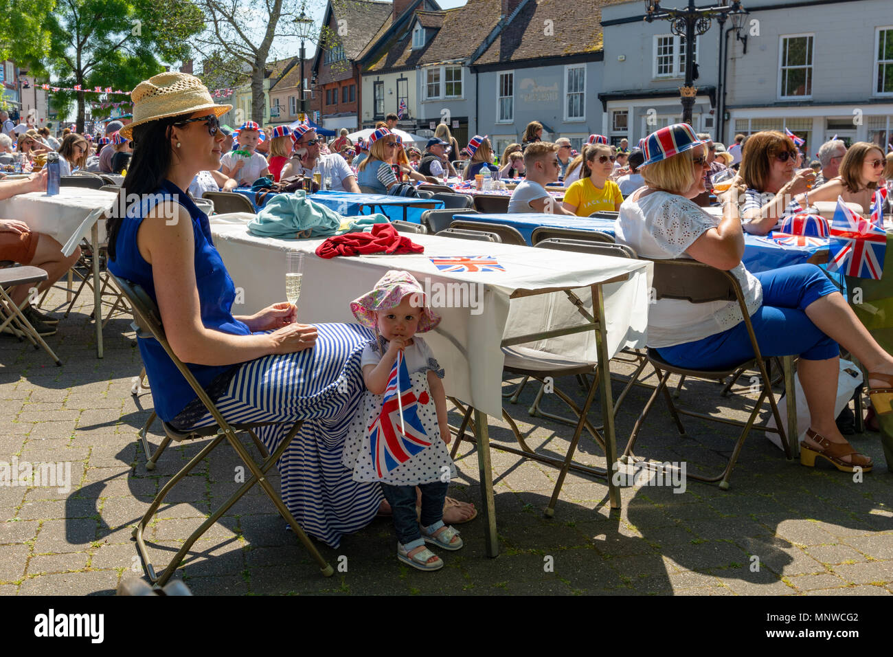 People watching the royal wedding of Prince Harry and Meghan Markle on a public outdoor screen in Ringwood, New Forest, Hampshire, England, UK, 19th May 2018. Young girl chewing on a Union Jack flag. Stock Photo