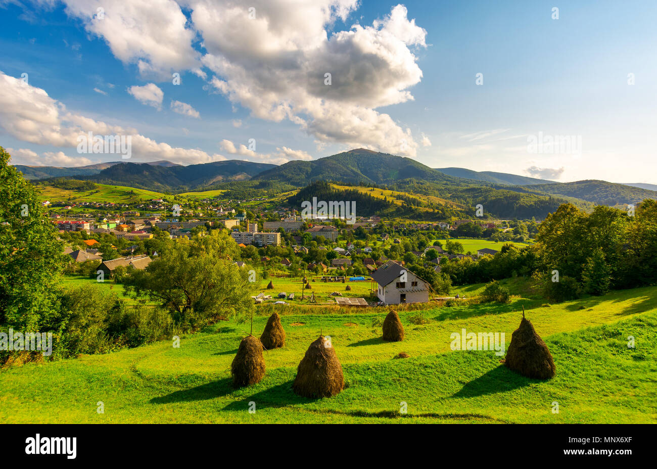 beautiful rural landscape in mountains. haystacks on the grassy hills. village at the foot of the mountain. interesting cloud formation over the ridge Stock Photo