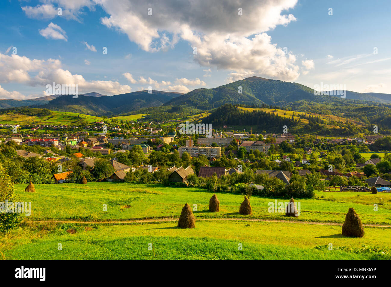 beautiful rural landscape in mountains. haystacks on the grassy hills. village at the foot of the mountain. interesting cloud formation over the ridge Stock Photo