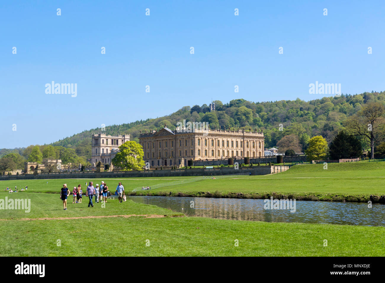 Visitors walking alongside the River Derwent in Chatsworth Park with Chatsworth House behind, Chatsworth, Derbyshire, England, UK Stock Photo